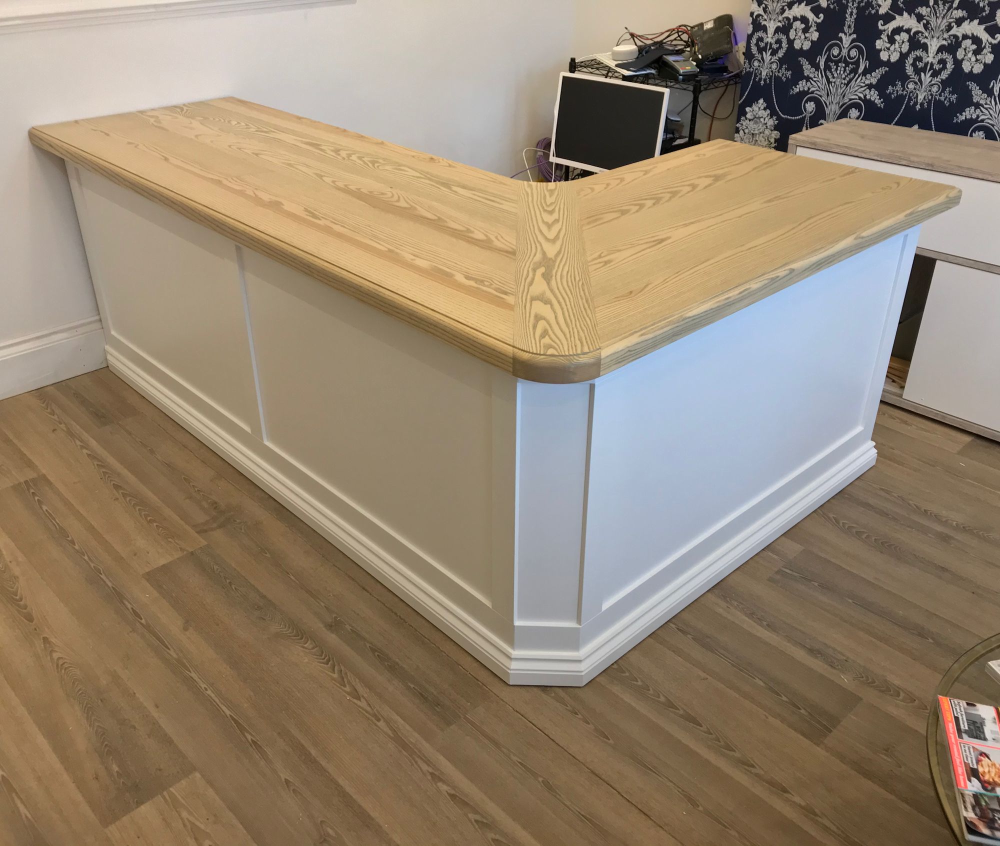 L-shaped reception counter with a solid ash top and white panelled base