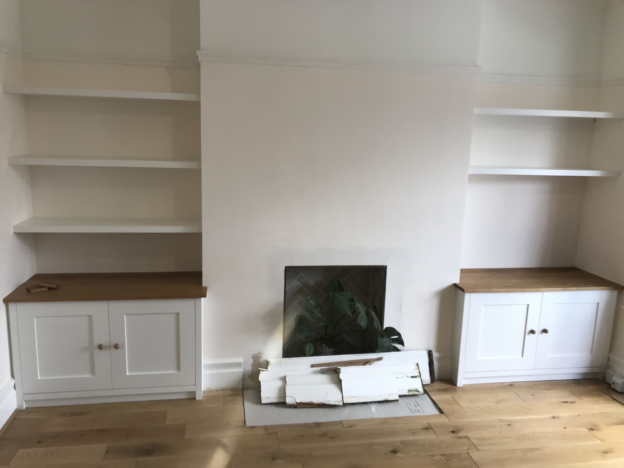 Painted alcove cupboards with oak tops and floating shelves either side of a chimney breast