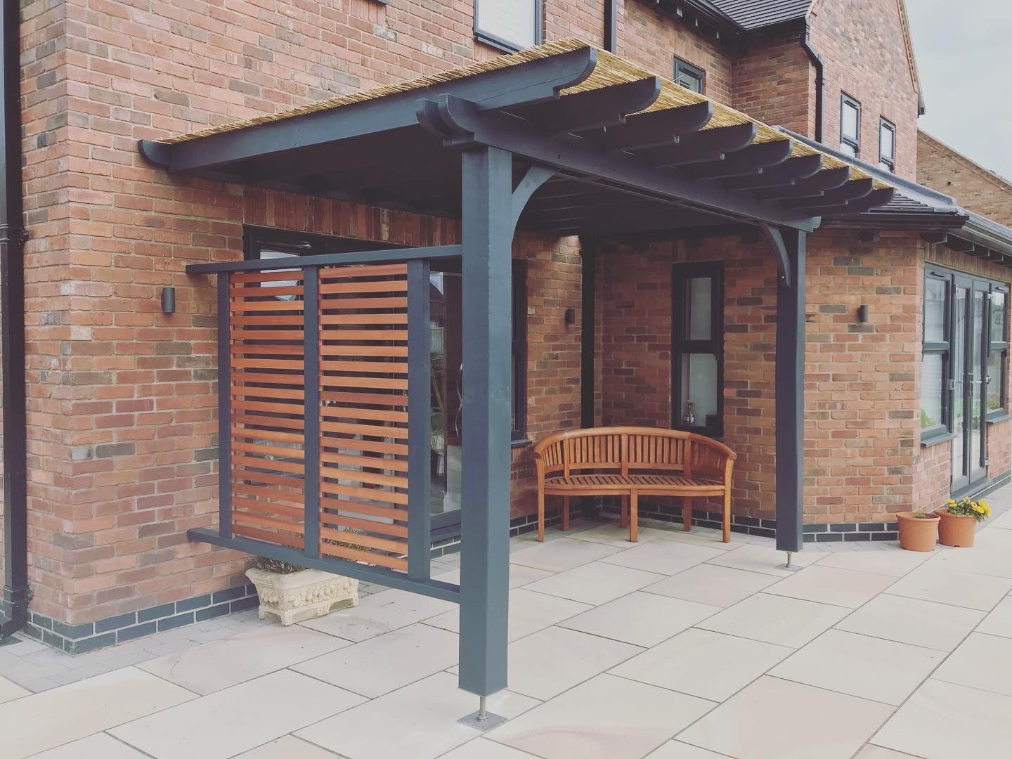 Charcoal painted pergola with a reed roof and hardwood slatted privacy screen