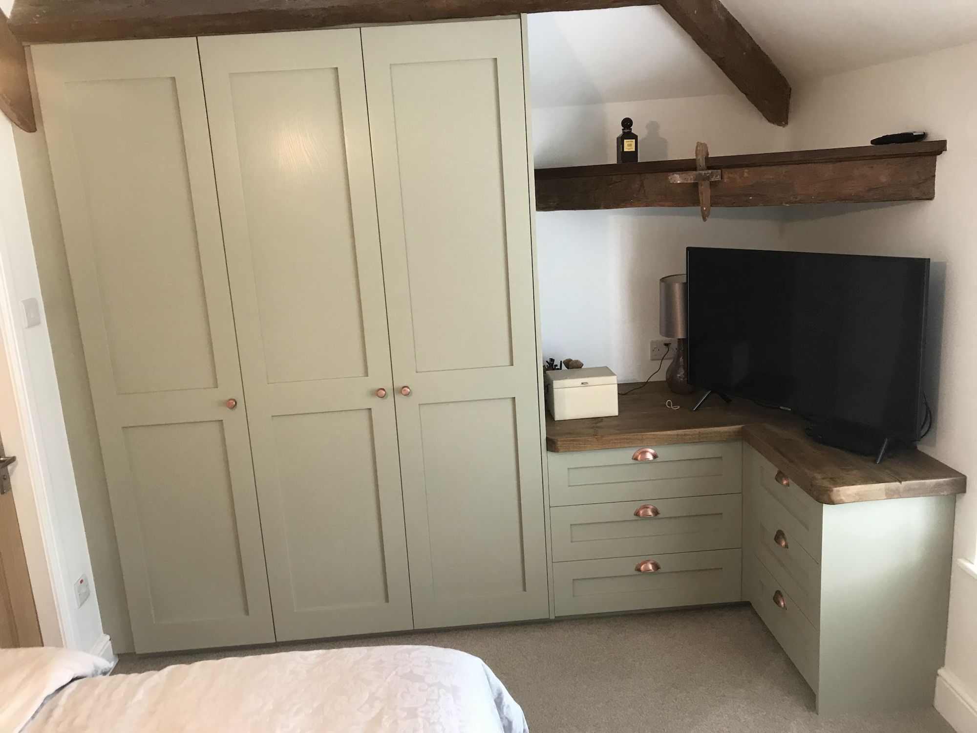 Sage green shaker fitted wardrobes and corner drawers with a rustic timber top under exposed beams