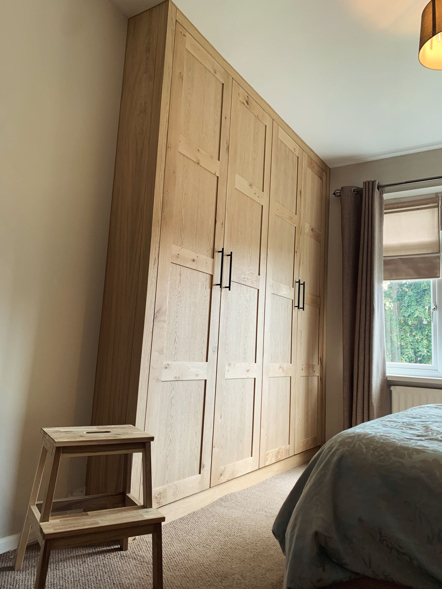 Rustic oak four-door shaker wardrobe built floor to ceiling in a bedroom