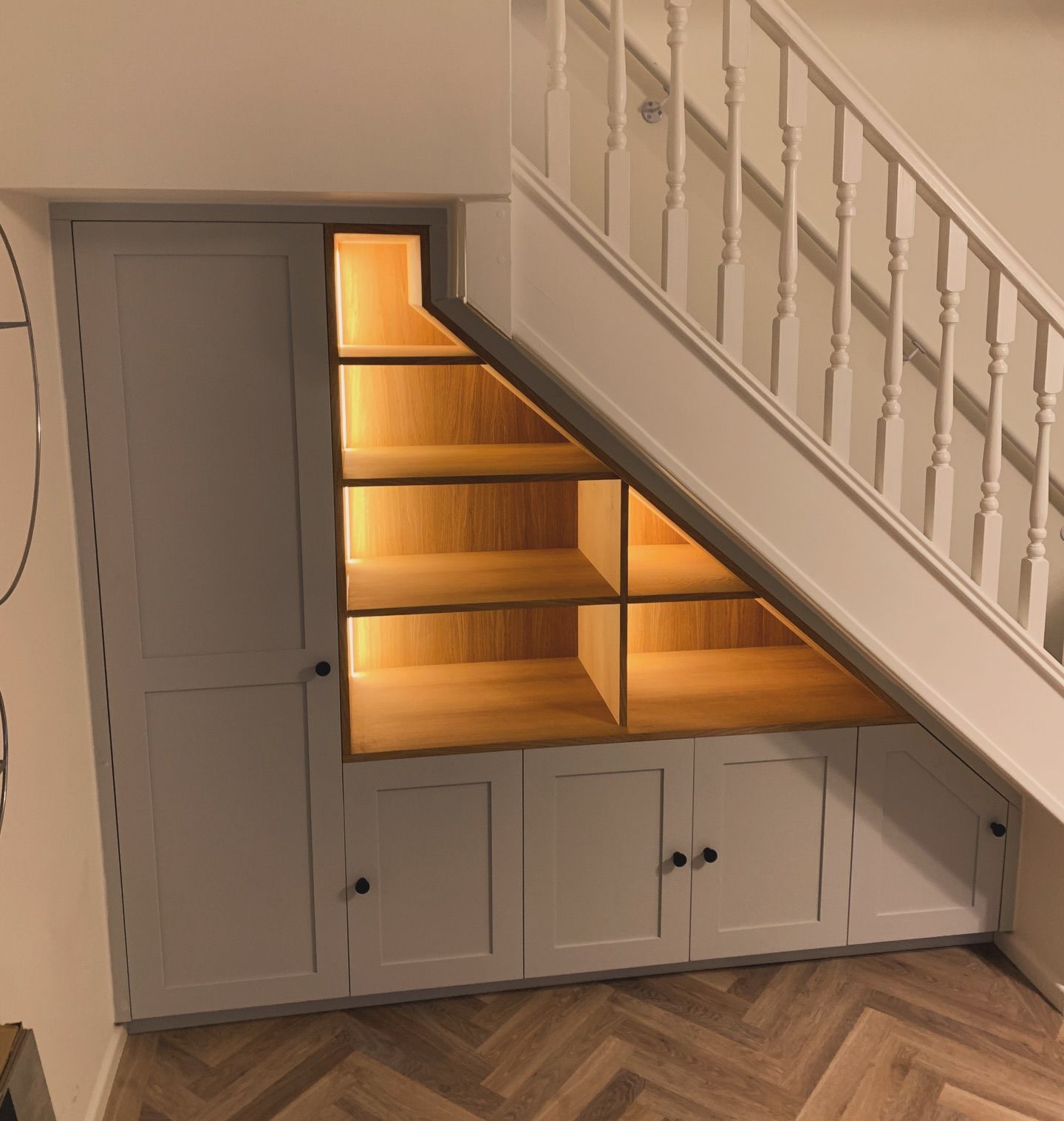 Under-stairs unit with grey shaker cupboards and open oak shelving lit with LED strips